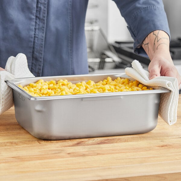 A Vollrath stainless steel hotel pan filled with macaroni and cheese on a counter in a professional kitchen.