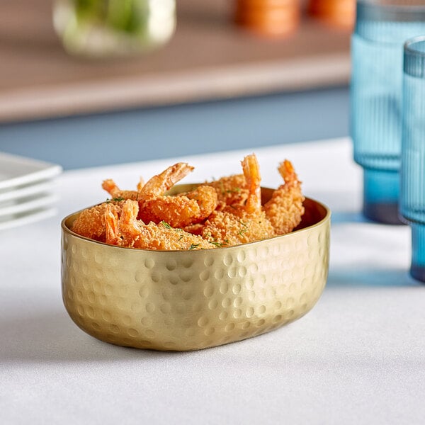 An oval serving bowl of fried shrimp on a table with a blurry green background.
