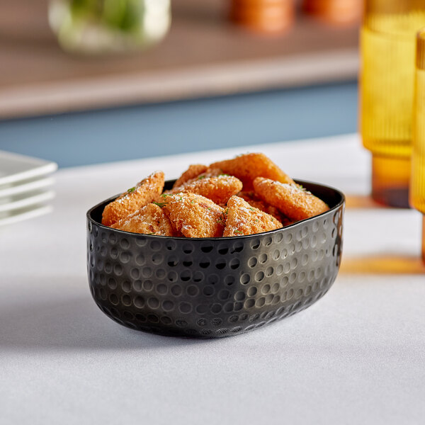 An American Metalcraft black hammered aluminum oval serving bowl filled with food on a table.