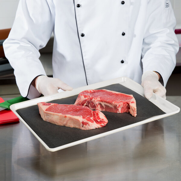 A chef holding a white tray with raw meat.