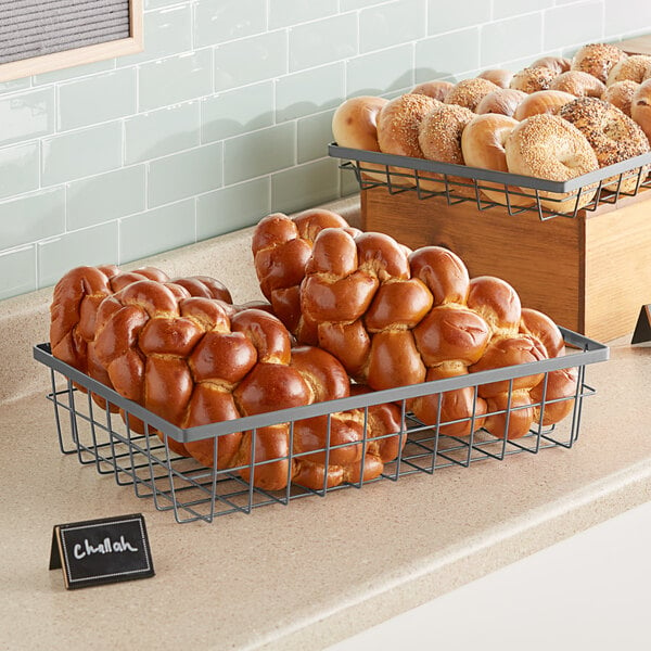 A counter with GET Enterprises Urban Renewal rectangular wire baskets of bread and pastries on a counter in a bakery display.