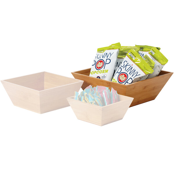Three square bamboo bowls with liners holding candy, popcorn, and snacks.