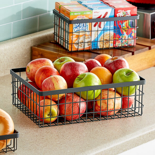 A metal gray rectangular wire basket filled with apples and oranges on a counter.