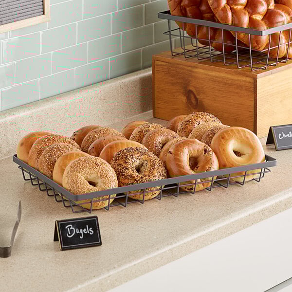 A tray of bagels in a GET Urban Renewal metal gray rectangular wire basket on a bakery counter.