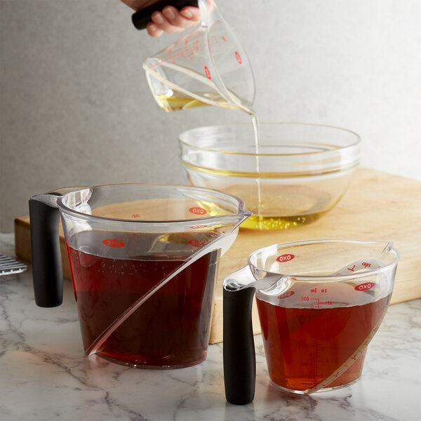 A hand pouring brown liquid into an OXO Good Grips clear measuring cup.