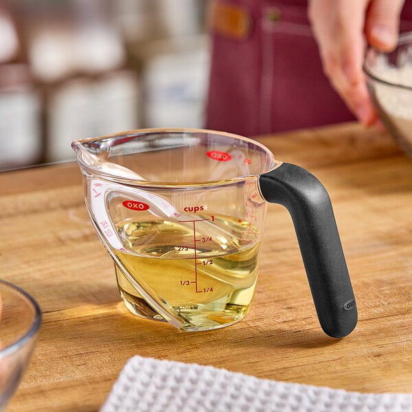 A person using an OXO measuring cup to pour yellow liquid.