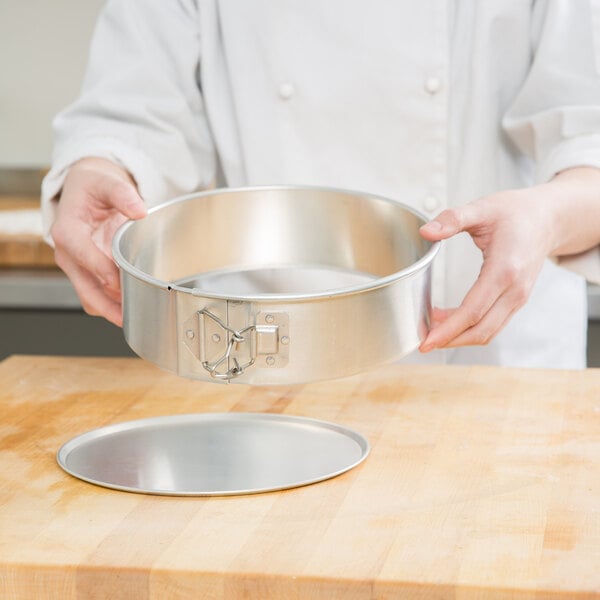 A person holding a Chicago Metallic round aluminum cake pan over a wooden surface.