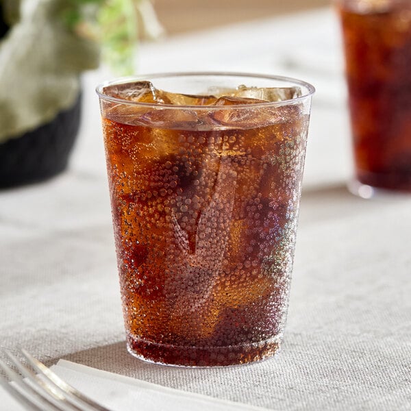 A clear hard plastic tumbler filled with a dark carbonated beverage and ice.