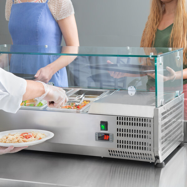 A woman serving food in a Avantco countertop refrigerated prep rail.