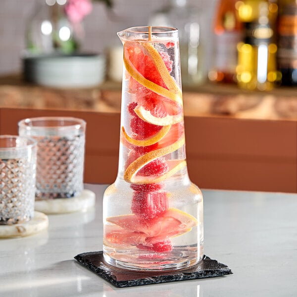 An American Metalcraft glass carafe filled with water and fruit on a table.