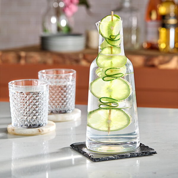 An American Metalcraft glass carafe filled with water and lime slices on a counter.