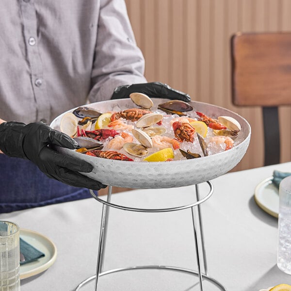 A round silver hammered aluminum seafood tray filled with assorted seafood and ice, displayed on a metal stand.