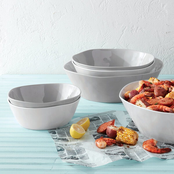 A stack of white American Metalcraft melamine bowls with shrimp, sausage, and corn on newspaper.