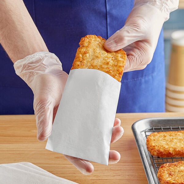 A person in gloves holding a Carnival King hash brown bag full of food.