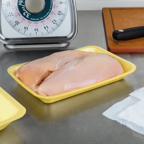 A yellow CKF foam meat tray with raw chicken breasts on a counter.