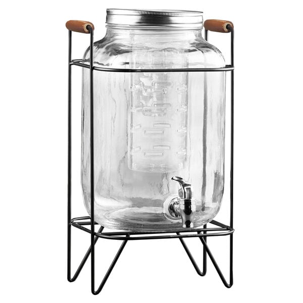 A Stylesetter clear glass beverage dispenser with a black metal stand.