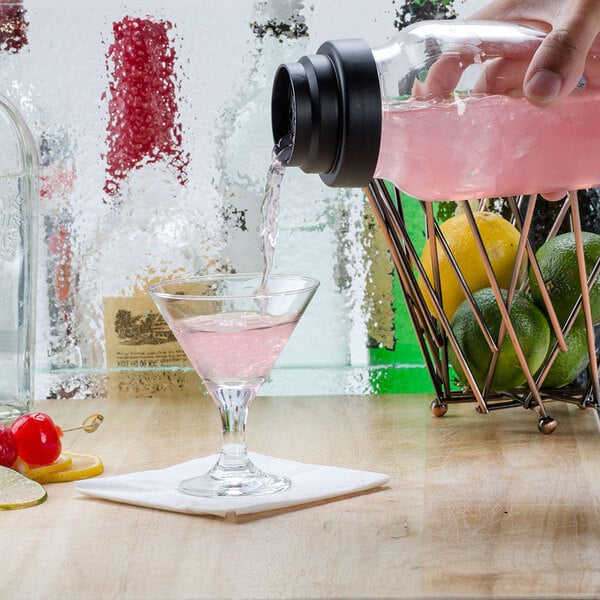 A hand using a Libbey Cobbler cocktail shaker to pour a pink drink into a glass.