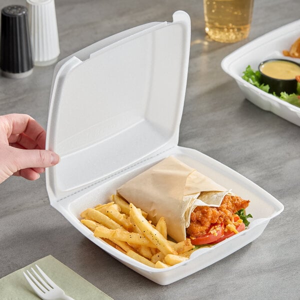 A white foam square take out container with a perforated hinged lid, holding a sandwich wrap and French fries.