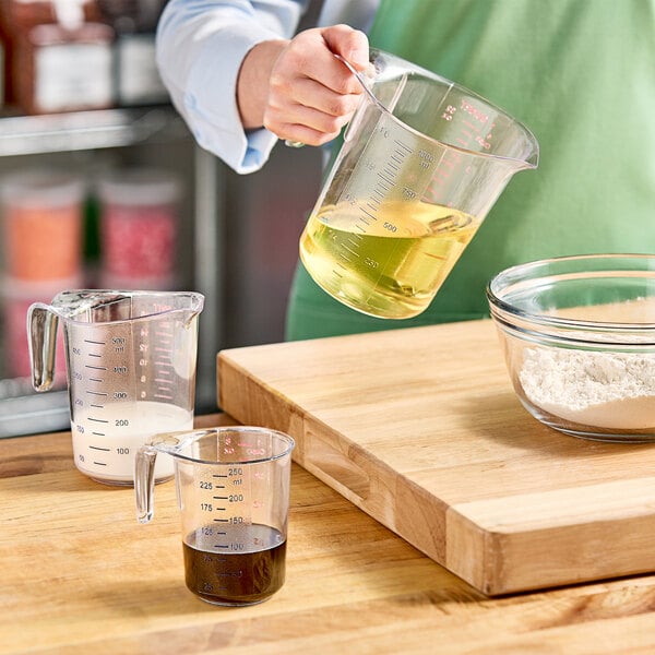 A person holding a Choice clear plastic measuring cup with yellow liquid.