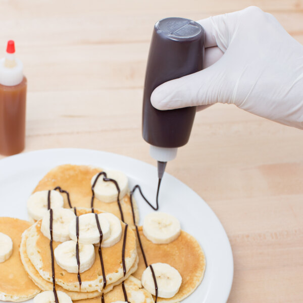 A small plastic squeeze bottle being used to drizzle sauce over pancakes with banana slices.