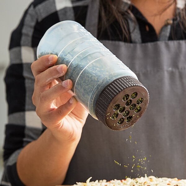 A woman using a Vollrath brown shaker lid to season a pizza.