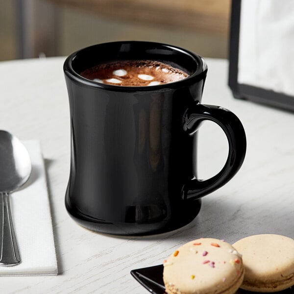 A black Acopa Victor stoneware mug with a drink and cookies on a table.