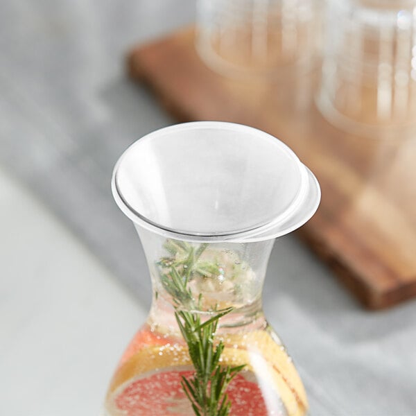 A Libbey clear plastic carafe lid on a glass carafe with a drink inside.