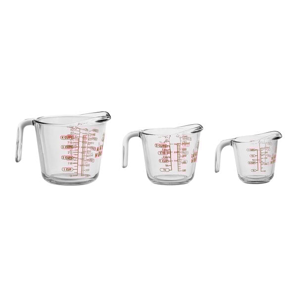 A group of three clear glass Anchor Hocking measuring cups with red writing on them.