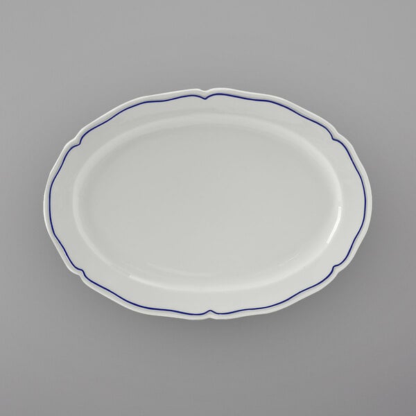 A white Tuxton china oval platter with scalloped edges and blue trim.