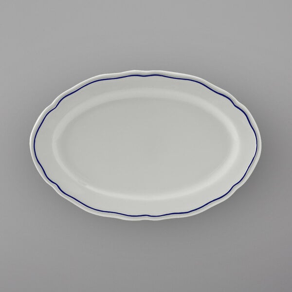 A white Tuxton oval platter with scalloped edges and blue trim.