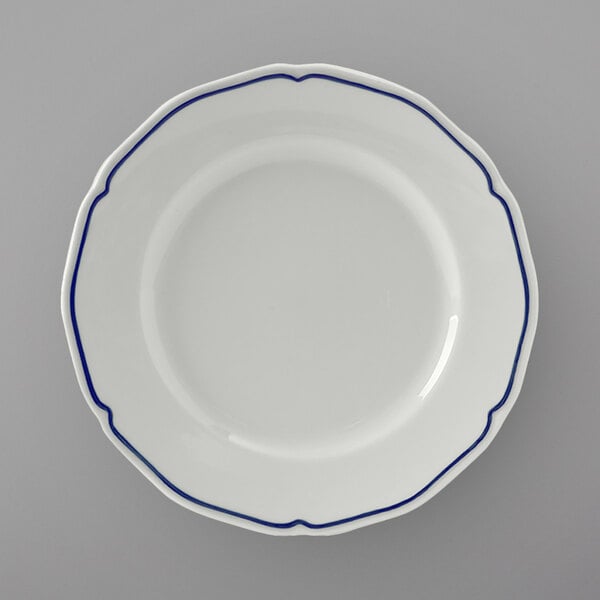 A close up of a Tuxton white china bread and butter plate with a scalloped edge and blue trim.