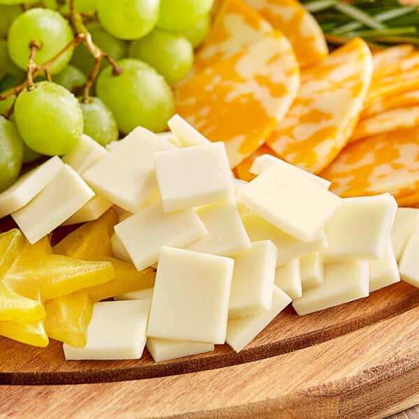 A wooden cutting board with a solid block of Savoldi whole milk mozzarella cheese, grapes, and green fruit.