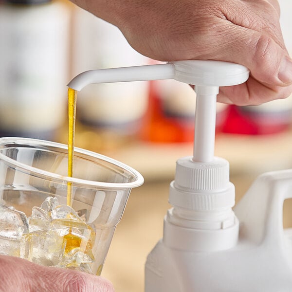 A person using a Choice Universal syrup pump to pour liquid into a glass of ice.