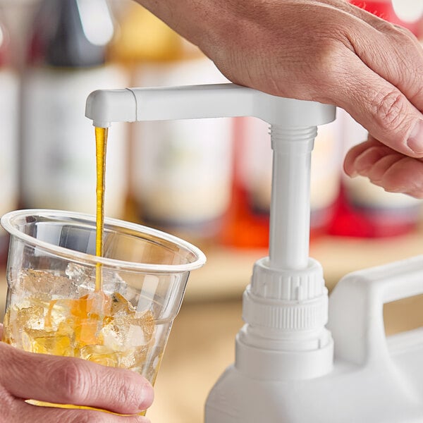 A hand using a white Choice condiment pump to pour a drink into a plastic cup.