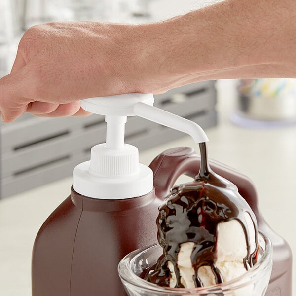 A hand using a Choice chocolate syrup pump to pour syrup over a scoop of ice cream.