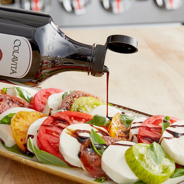 A bottle of Colavita Balsamic Glaze being poured over a plate of tomatoes, cheese, and basil.
