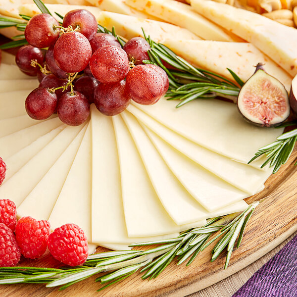 A plate with a block of Walnut Creek Foods Monterey Jack Cheese, grapes, and figs.