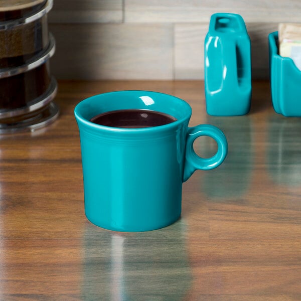 A turquoise Fiesta china mug with a handle full of a drink on a wood surface.