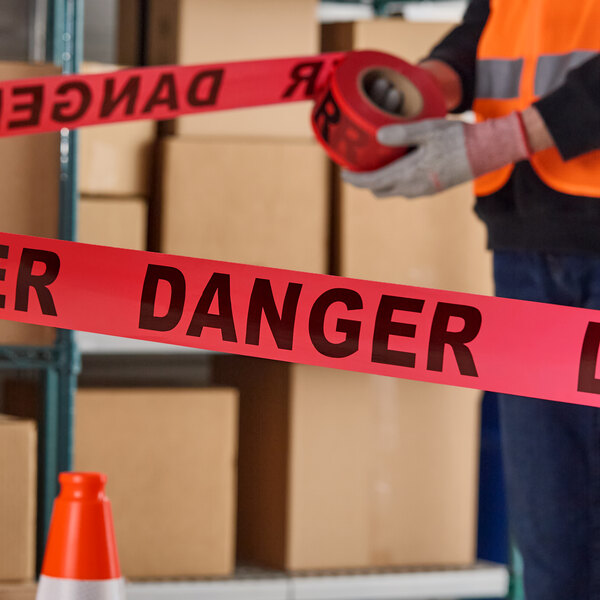A roll of red 'DANGER' tape being used in a warehouse setting.