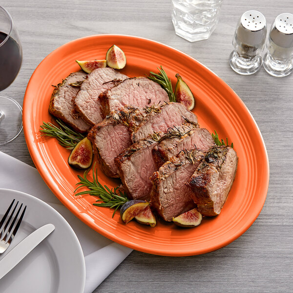 A Tuxton oval china platter with steak and a glass of wine on a table.