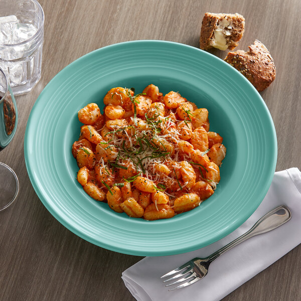 A bowl of pasta with a fork on a table with a glass of wine.