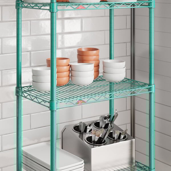A green wire shelf unit with stacked bowls, plates, and a utensil holder, shown in a kitchen setting.