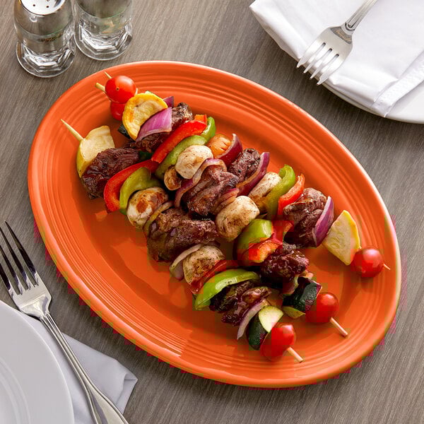 A Tuxton oval china platter with skewers and vegetables on it.