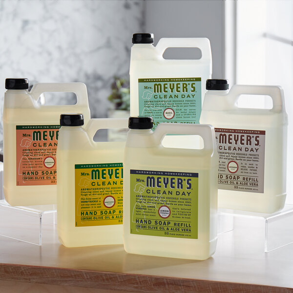 A group of white plastic Mrs. Meyer's Lemon Verbena hand soap refill bottles with black lids.