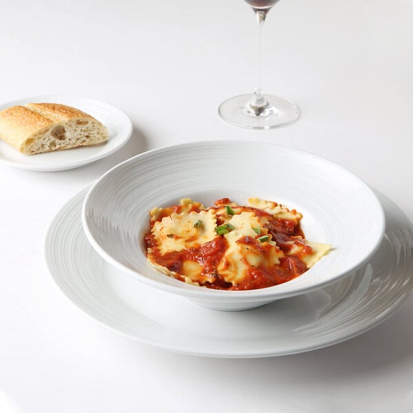 A Tuxton Pacifica bright white china plate with a bowl of pasta and a glass of wine.