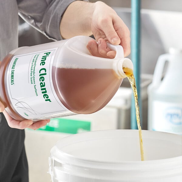 A person pouring a jug of Advantage Chemicals concentrated pine cleaner into a bucket.