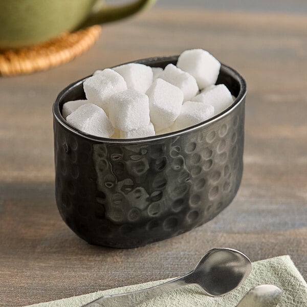 An American Metalcraft black hammered aluminum bowl holding sugar cubes on a table.