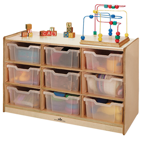 A Whitney Brothers wooden storage cabinet with plastic bins on shelves holding toys.