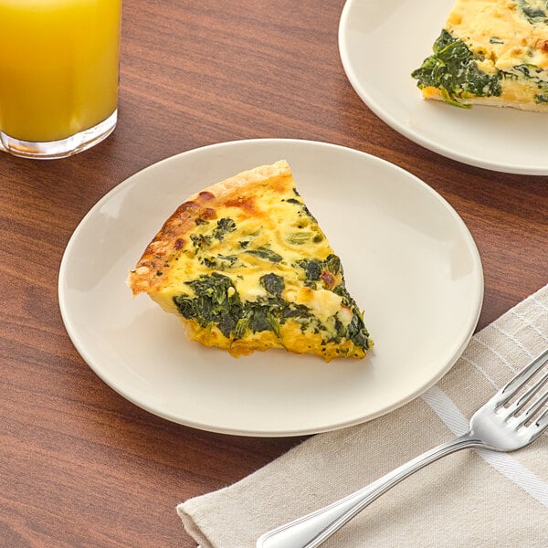 A slice of quiche on an Acopa ivory stoneware plate with a fork.