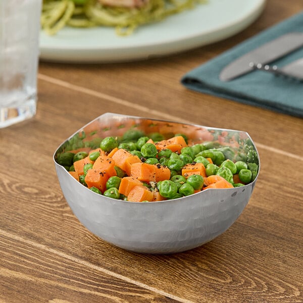 A round hammered stainless steel serving bowl filled with peas and diced carrots.